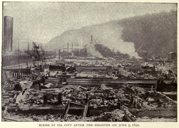 Schwarzes und weißes Foto einer Stadtlandschaft nach einer Katastrophe am 5. Juni 1892, das Gebäude, Strommasten, Rauch und einen Hügel im Hintergrund zeigt, mit Text unten.