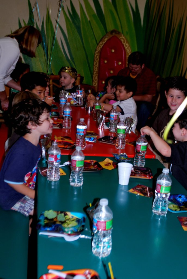 Eine Gruppe von Kindern sitzt um einen Tisch und isst Snacks auf einer Geburtstagsparty.