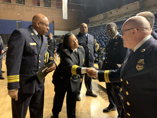 Eine Gruppe uniformierter Personen, die Hände schütteln, vor sitzenden und stehenden Zuschauern, mit einem Banner im Hintergrund, das "Feuerwehrchef und -offizier des Jahres" trägt.