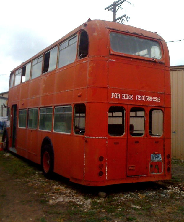 Ein roter Doppeldeckerbus steht vor einer Scheune und einem Strommast.