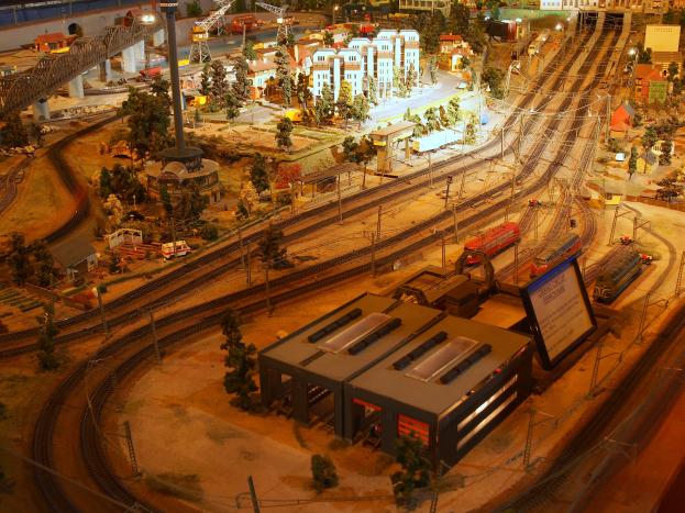 Eine Modellbahnanlage in einem Museum mit Miniaturgebäuden, Bäumen, Fahrzeugen und anderen Gegenständen, die eine belebte Stadtlandschaft schaffen.