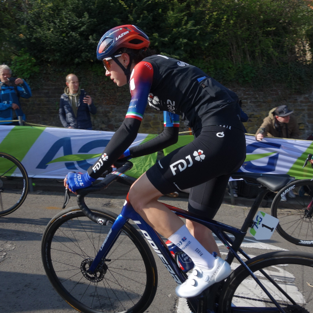Die professionelle Radrennfahrerin Katie Archibald fährt auf einem Fahrradstraße, trägt einen Helm, eine Brille, Handschuhe und Schuhe und hat eine Menschenmenge neben sich.