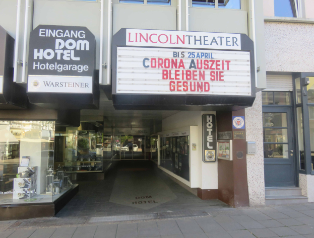 Das Lincoln Theater in Berlin, Deutschland, ein Gebäude mit Glasfenstern und -türen und einer Tafel mit Text darauf, das verschiedene Objekte im Inneren zeigt und so den Eindruck einer pulsierenden Stadtlandschaft vermittelt.