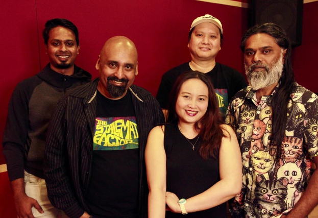 Eine Gruppe von Menschen, die zusammen in einem Aufnahmestudio stehen und vor einer roten Wand lächeln.