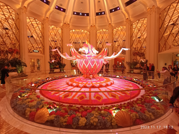 Ein geschäftiges Treiben im Bellagio Hotel und Casino in Las Vegas, Nevada, mit dekorativen Blumenarrangements auf dem Boden, Menschen mit Taschen und beleuchteten Säulen im Hintergrund.