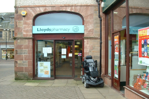 Apotheke mit einem vor dem Gebäude geparkten Auto und einem Gebäude auf der linken Seite.