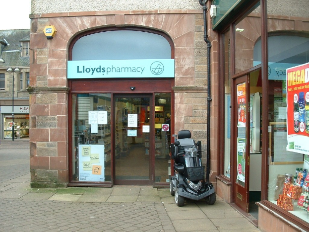 Apotheke mit einem vor dem Gebäude geparkten Auto und einem Gebäude auf der linken Seite.