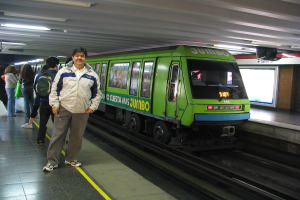 Ein Zug auf einem Bahngleis mit Menschen auf der linken Seite und einem Dach oben im Bild.