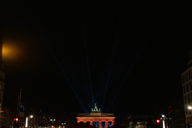 Das Brandenburger Tor in Berlin nachts, von Straßenlaternen beleuchtet, umgeben von Gebäuden, Bäumen, Pfählen, Verkehrszeichen, Schildern und Zelten unter einem dunklen Himmel.