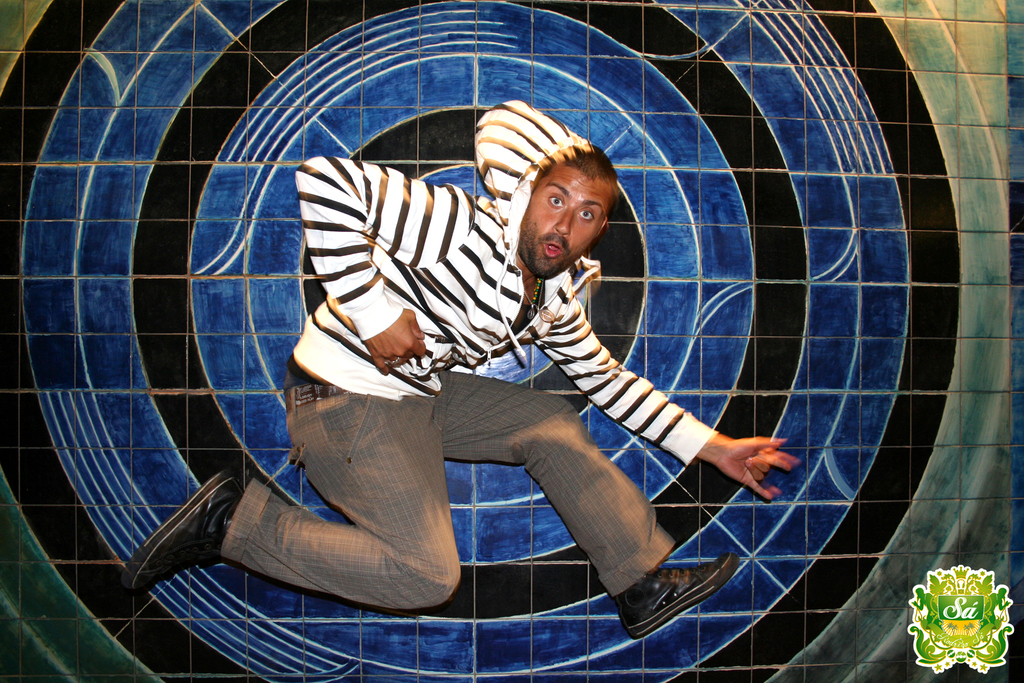 Ein Mann tanzt mit einem bunten Hintergrund und einem Logo mit Text in der rechten oberen Ecke.