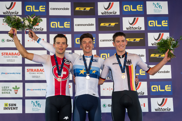 Drei Männer stehen auf einem Podest, jeder trägt eine Medaille und hält einen Blumenstrauß, im Hintergrund ist ein "Giro d'Italia"-Schild zu sehen.