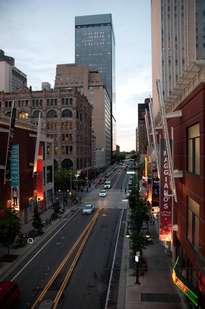 Eine Stadtansicht mit einer Straße voller Autos unten, flankiert von Gebäuden und Wolkenkratzern auf beiden Seiten und einem Himmel oben.
