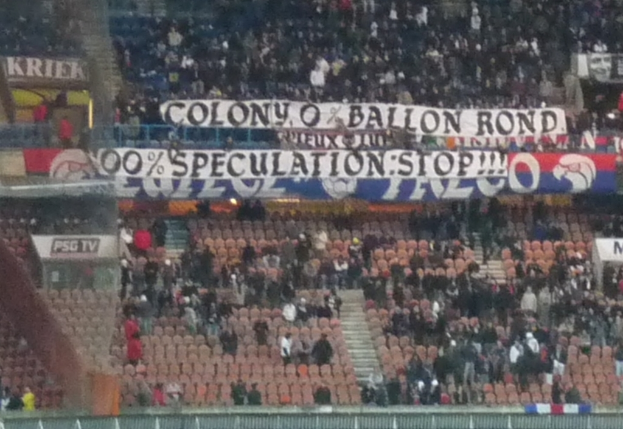 Ein Stadion voller großer Menge, Banner und Stühle, mit einem Zaun unten und Treppen auf der linken Seite.
