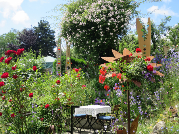 Ein Garten mit bunten Blumen und Pflanzen, mit einem Tisch mit einer Decke und Stühlen, umgeben von Bäumen unter einem bewölkten Himmel auf dem Chelsea Flower Show.