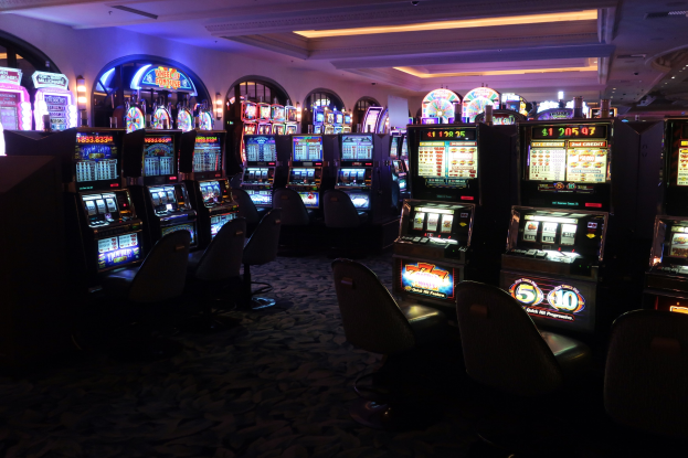 Reihe von Spielautomaten in einem Casino, jeder mit Text und Zahlen, die angeben, dass sie zum Verkauf stehen, begleitet von Stühlen und Deckenleuchten.