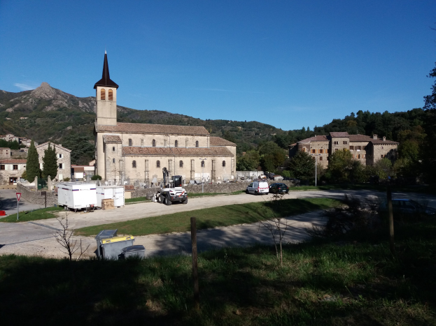 Luftaufnahme einer kleinen Stadt mit einer zentralen Kirche, umgeben von Gebäuden, Bäumen, Straßen, Fahrzeugen und Schildern, vor einem klaren blauen Himmel.