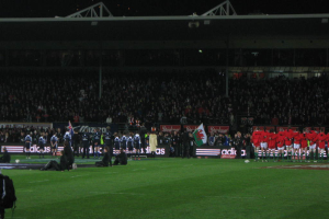 Ein Blick auf ein Sportereignis mit einem Eisengitter und Lautsprechern oben und einer Menge, Werbung, Flagge und Boden unten.
