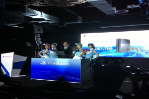 Menschen auf einer Bühne in der Nähe eines Rednerpults mit 'Playstation' darauf, mit einem Projektionsschirm an der Wand dahinter.