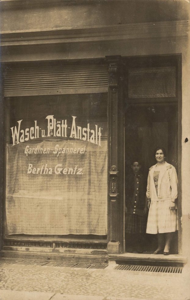 Eine Frau steht vor einem Geschäft mit einem Banner in Berlin, Deutschland, auf einem alten Schwarz-Weiß-Foto.