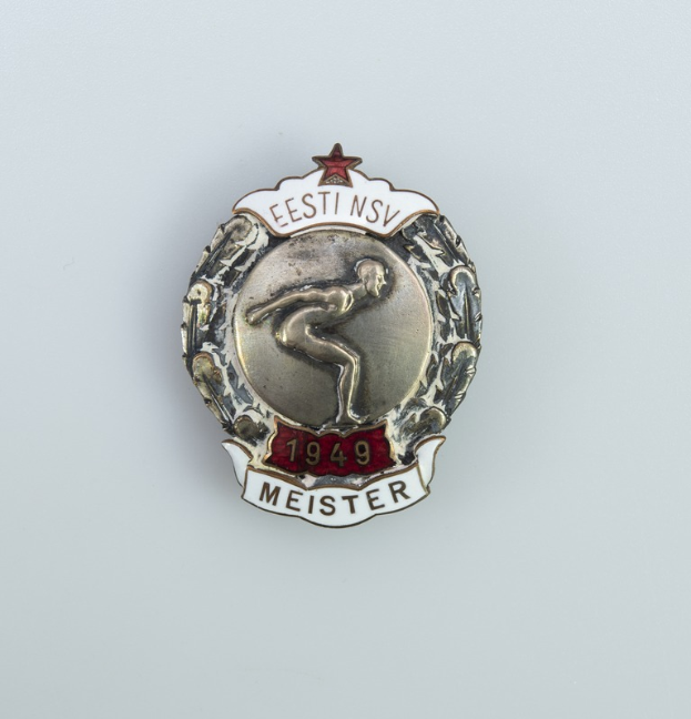 Ein silbernes Abzeichen mit einem roten Stern, Emblem der Olympischen Spiele 1949 in Deutschland, mit Text in der Mitte auf einem einfarbigen Hintergrund.