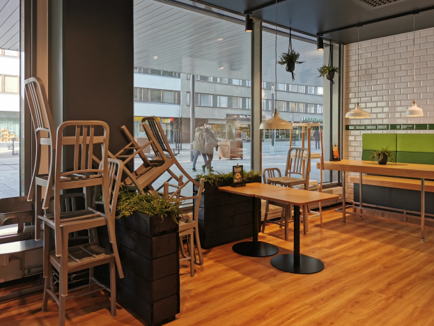 Ein Restaurantinnenraum mit hölzernen Tischen und Stühlen, ein großes Fenster mit einer Berliner Straßenszene, die Fußgänger, Gebäude und Straßenmöbel zeigt.