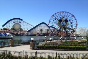 Luftaufnahme von Disney California Adventure mit seinem Riesenrad und Achterbahn, umgeben von Grünflächen und einem Gewässer unter einem klaren blauen Himmel.
