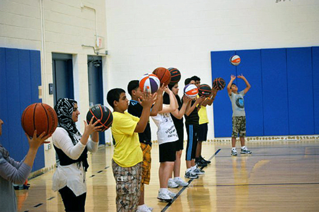 Eine Gruppe junger Menschen auf einem Basketballfeld, jeder hält einen Basketball in der Hand, mit Türen und einer Wand im Hintergrund.