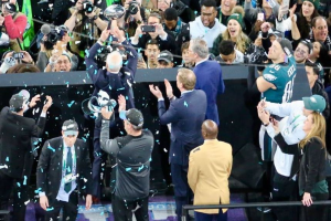 Philadelphia Eagles Spieler feiern mit dem Vince Lombardi Trophy nach dem Sieg im Super Bowl, einige tragen Mützen und halten den Pokal, während andere Konfetti werfen.