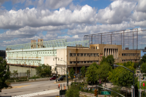 Eine breite Straße mit Fahrzeugen, gesäumt von Bäumen und Straßenlaternen, führt zu einem großen Gebäude in der Nähe eines Gewässers.