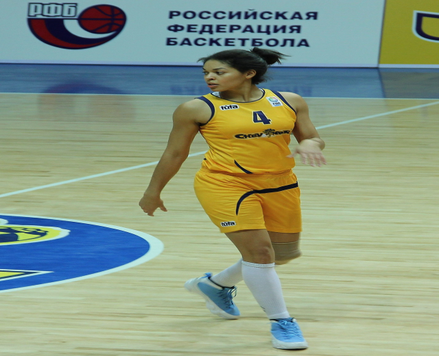 Ein professioneller Basketballspieler in gelber Uniform, der auf einem Court dribbelt, mit einer Tafel im Hintergrund.