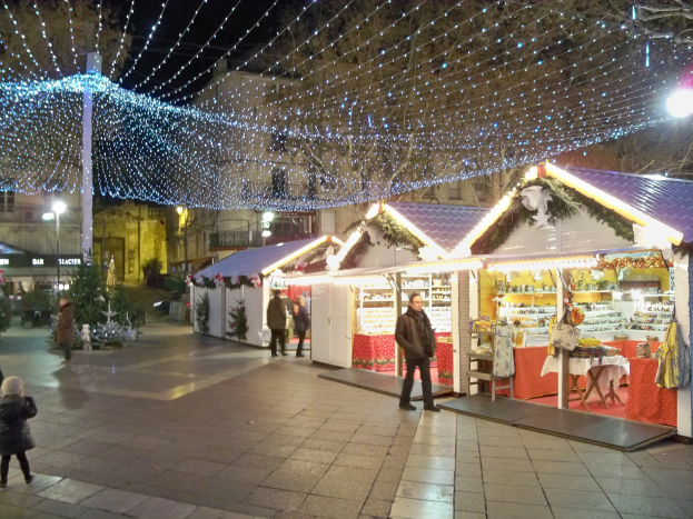 Eine belebte Stadtstraße bei Nacht mit Menschen, Fahrzeugen, Fahrrädern, Gebäuden, Laternenmasten, Ampeln und einem Uhrenturm, beleuchtet von Weihnachtslichtern.