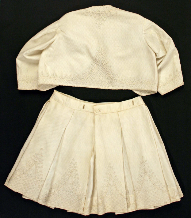 Ein weißes, langärmeliges Kleid mit einer gerafften, bodenlangen Schleppe auf einem weißen Hintergrund, das eine hohe Taille, voluminösen Stoff und einen dezenten Glanz aufweist.