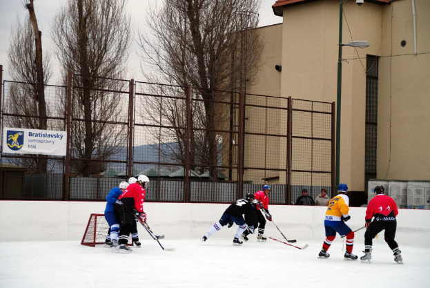 Menschen spielen Eisstockschießen auf einer Eisbahn mit Gebäuden, Bäumen und einer Straßenlaterne im Hintergrund.
