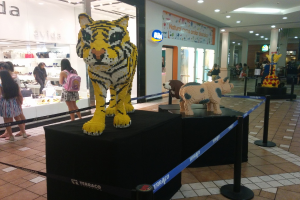 Statuen von Tieren auf schwarzen Kisten umgeben von Pfosten mit Gummibändern, mit Geschäften, die Taschen, Schuhe und andere Gegenstände anbieten, und Menschen, die herumlaufen, unter Deckenlampen.