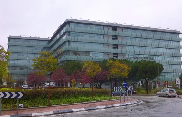 Großes modernes Gebäude mit zahlreichen Fenstern, umgeben von Grünflächen und städtischen Elementen, als Hauptsitz der Europäischen Zentralbank identifiziert.