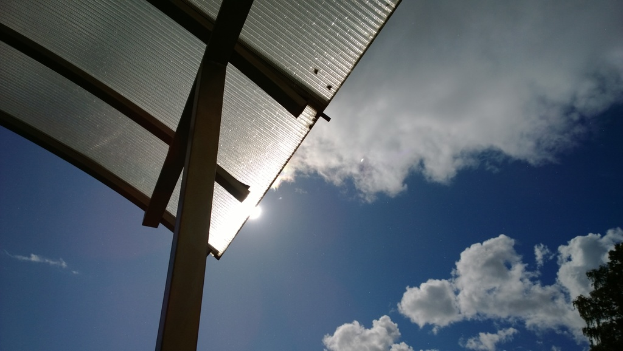 Ein Dach, das mit Asbestplatten bedeckt ist, mit einem bewölkten Himmel darüber und Bäumen auf der rechten unteren Seite.