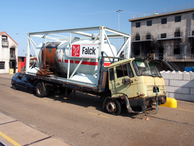 Ein Betonmischer-Lkw steht am Straßenrand neben Gebäuden mit Fenstern, Geländern und Treppen unter einem klaren blauen Himmel mit Laternen im Hintergrund.