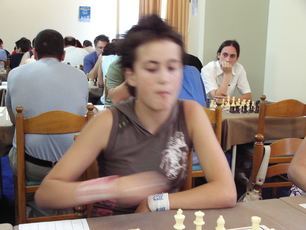 Ein Raum mit Menschen an Tischen Schach spielend, mit einer Vorhangwand und einem Foto in der rechten Ecke.