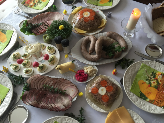 Ein lang gedeckter Tisch mit verschiedenen Speisen, Besteck, Glaswaren und Kerzen, umgeben von Stühlen, was auf ein traditionelles deutsches Osteressen hinweist.