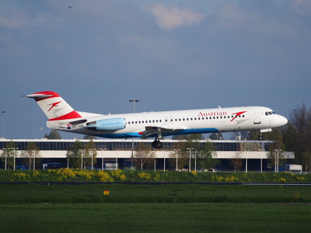 Ein Airbus A320-200 der Austrian Airlines beim Start am Frankfurter Flughafen, mit Grünfläche, Gebäuden und bewölktem Himmel im Hintergrund.